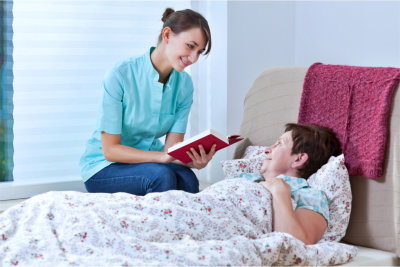 Helpful nurse reading book while patient was lying in bed