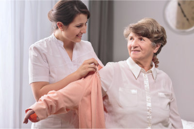Helpful young caregiver giving the sweater to older woman
